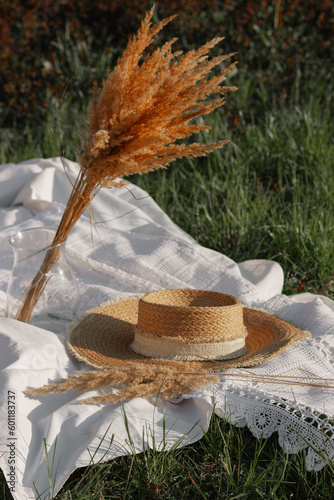 Retro straw hat with dry pampas grass on white sheet with weaving lace among green grass of spring meadow. Boho style.