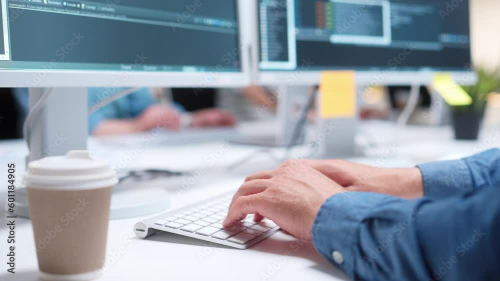 Close-up view of IT programmer typing code or creating software on white keyboard. Cup with coffee standing on table. Man using computers and working at office. Technology concept.
