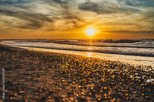 lowniczy zachód słońca nad morzem w miejscowości Sarbinowo. Promienie słońca malują wspaniałe odcienie złota na mokrym piasku plaży, tworząc magiczną atmosferę. 