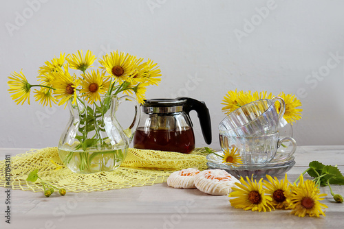 Summer still life: bouquets of yellow daisies in glass vases, yellow lace napkin, teapot on a gray background, space for text