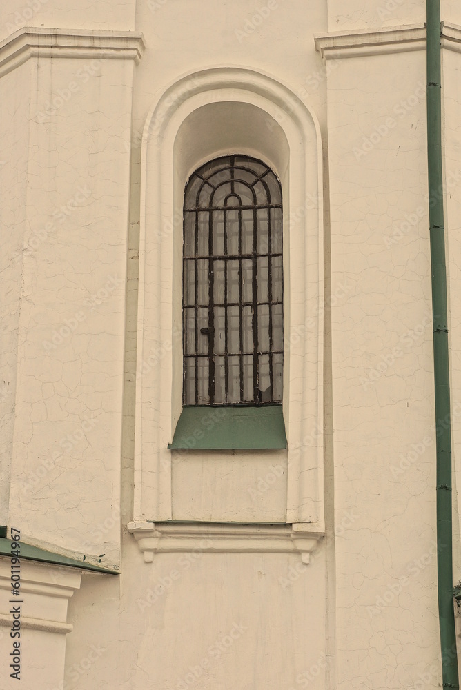 one old window behind a black iron grate on a white stone wall of a building on the street