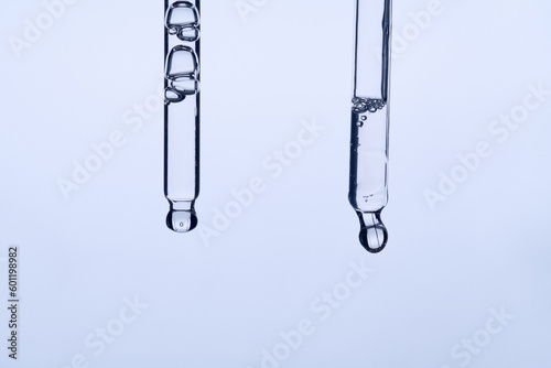 Two pipettes with facial serum on blue background. Liquid gel or essential oil with bubbles macro. Anti aging cosmetic product with hyaluronic acid closeup. Innovation technology concept. Front view.
