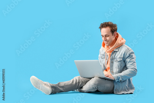 Male student with laptop on blue background
