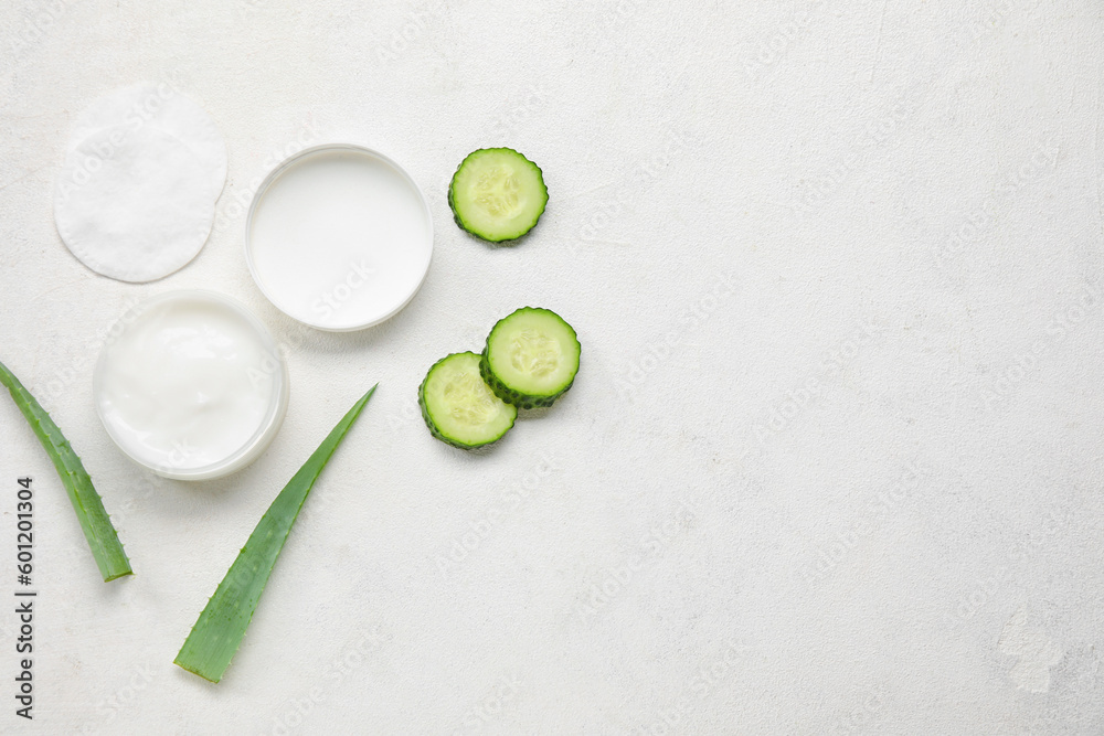Composition with jar of natural cream, cotton pads, aloe leaves and cucumber on light background Composition with jar of natural cream, cotton pads, aloe leaves and cucumber on light background