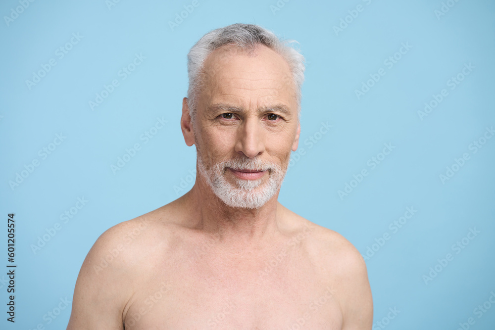 Confident portrait of senior handsome man smiles at camera, standing bare shoulders, blue background Confident portrait of senior handsome man smiles at camera, standing bare shoulders, blue background