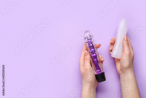 Woman holding vibrator and bottle of lubricant on lilac background