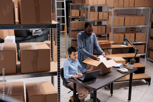 Diverse storehouse workers putting client order in carton box wrapped package in bubble wrap, preparing for delivery. Manager discussing shipping detalies with supervisor while working in warehouse photo