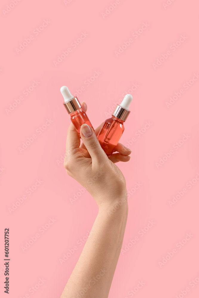 Hand holding cosmetic products on pink background Hand holding cosmetic products on pink background