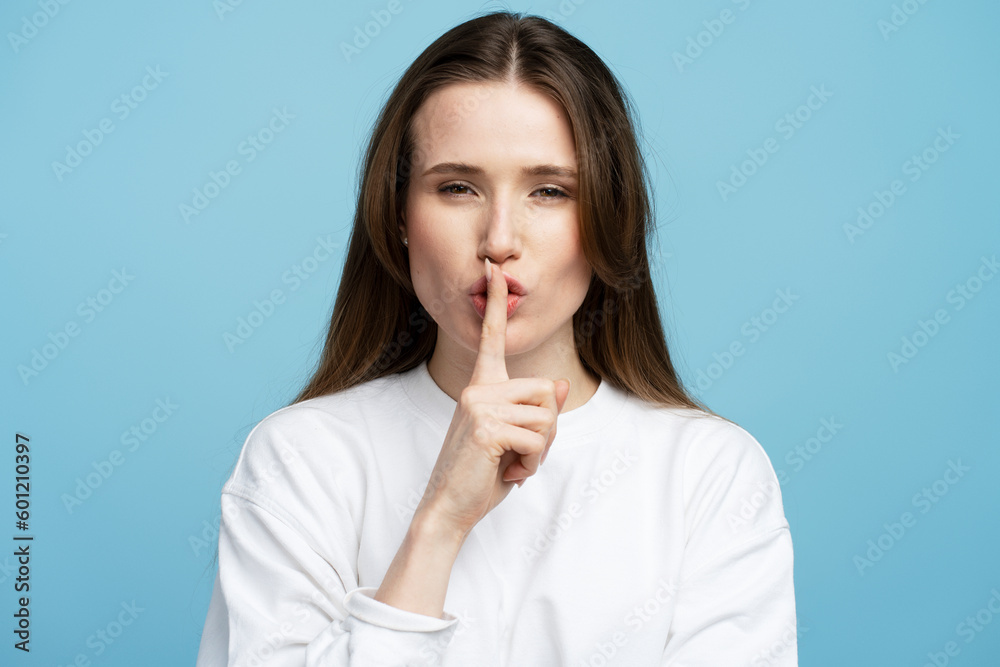 Young woman wearing white shirt putting her index finger at her lips in sign of silence Young woman wearing white shirt putting her index finger at her lips in sign of silence