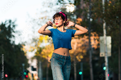 bella mujer adolescente estilo 80s 90s andando en skate en la ciudad, con maquillaje, anteojos y jeans. en un día soleado al atardecer.