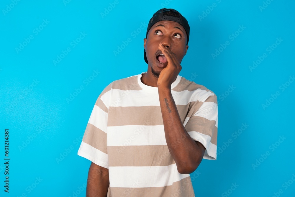 Handsome man wearing striped t-shirt and cap over blue background hear incredible private news impressed scream share Handsome man wearing striped t-shirt and cap over blue background hear incredible private news impressed scream share