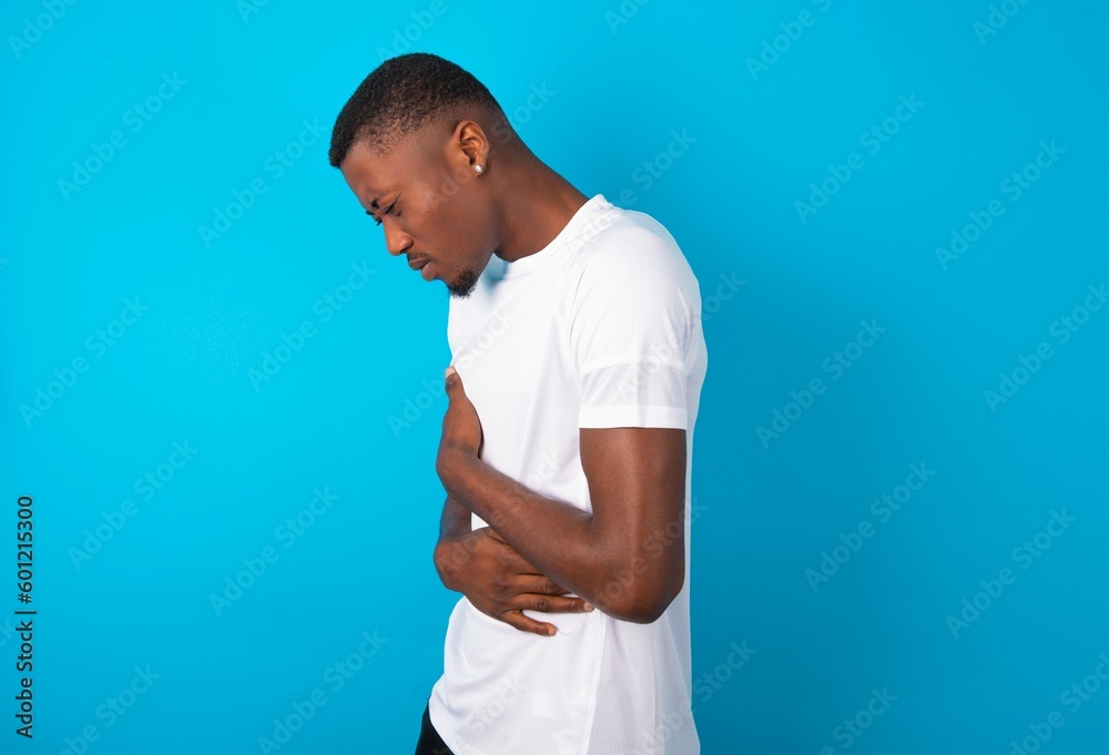 Handsome man wearing white T-shirt over blue background got stomachache Handsome man wearing white T-shirt over blue background got stomachache