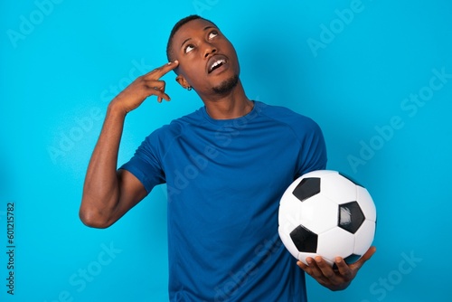 Fényképezés Young man wearing sport T-shirt holding a ball over blue background foolishness around shoots in temple with fingers makes suicide gesture