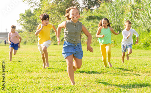 Group of happy children running on green grass on field.