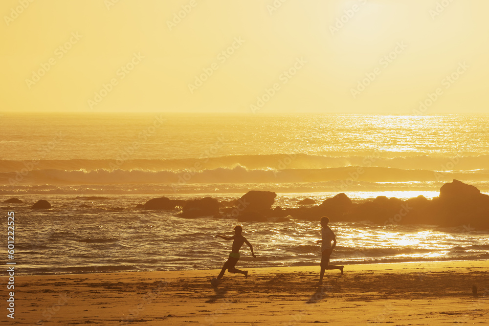 Teenage boys playing ball on the beach at sunset Teenage boys playing ball on the beach at sunset