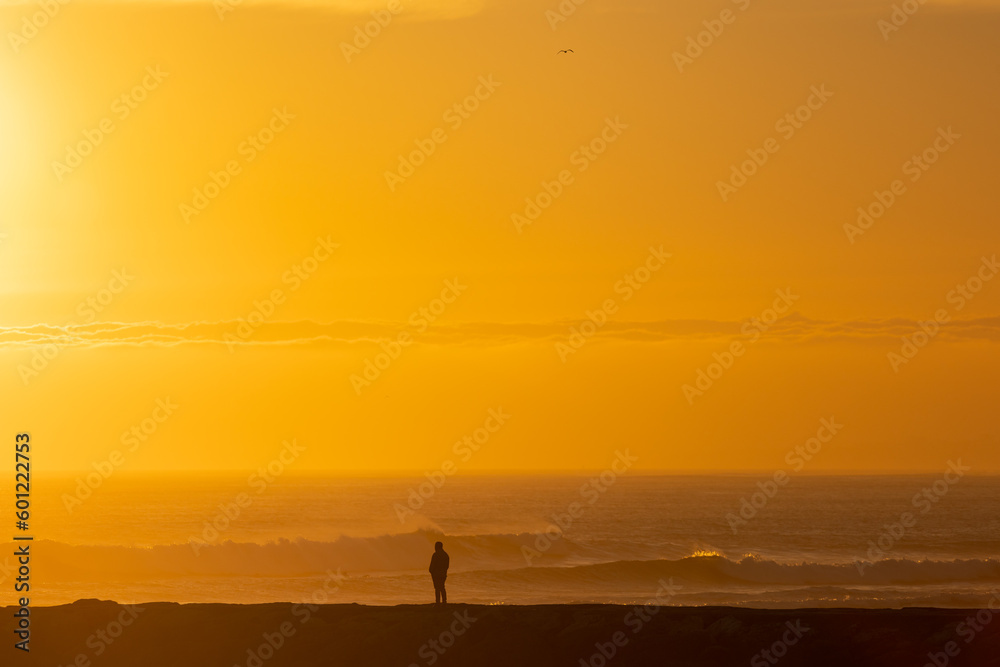 A lonely man stands by the sea at bright orange sunset