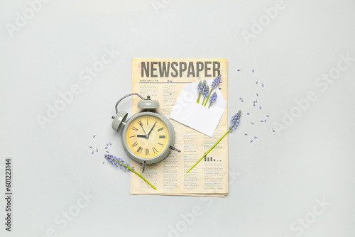Composition with beautiful Muscari flowers, alarm clock and newspaper on grey background