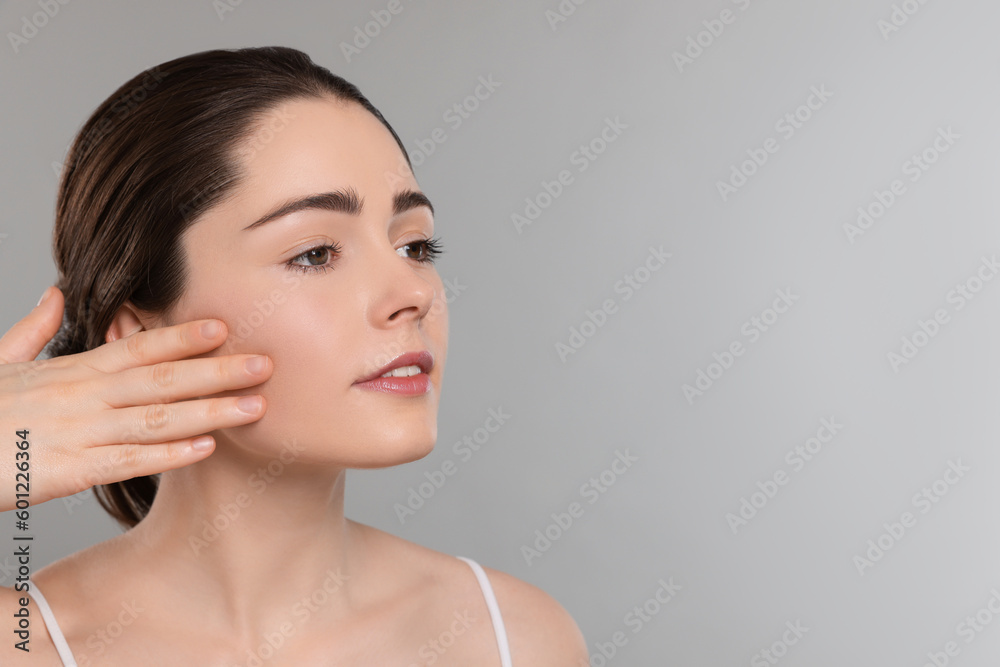 Young woman massaging her face on grey background. Space for text