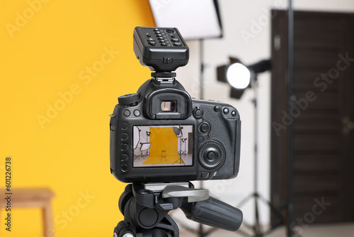 Tripod with camera  bar stool and professional lighting equipment in modern photo studio  focus on screen