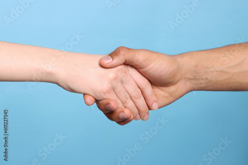 International relationships. People holding hands on light blue background, closeup