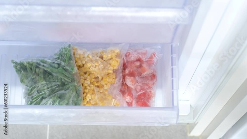 Female hand puts plastic bags with vegetables in freezer drawer. photo