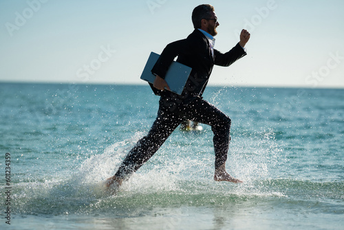 Fototapeta Naklejka Na Ścianę i Meble -  Excited businessman in wet suit run in sea. Funny business man, crazy comic business concept. Remote online working. Crazy summer business. Fun business lifestyle. Funny freelance businessman.
