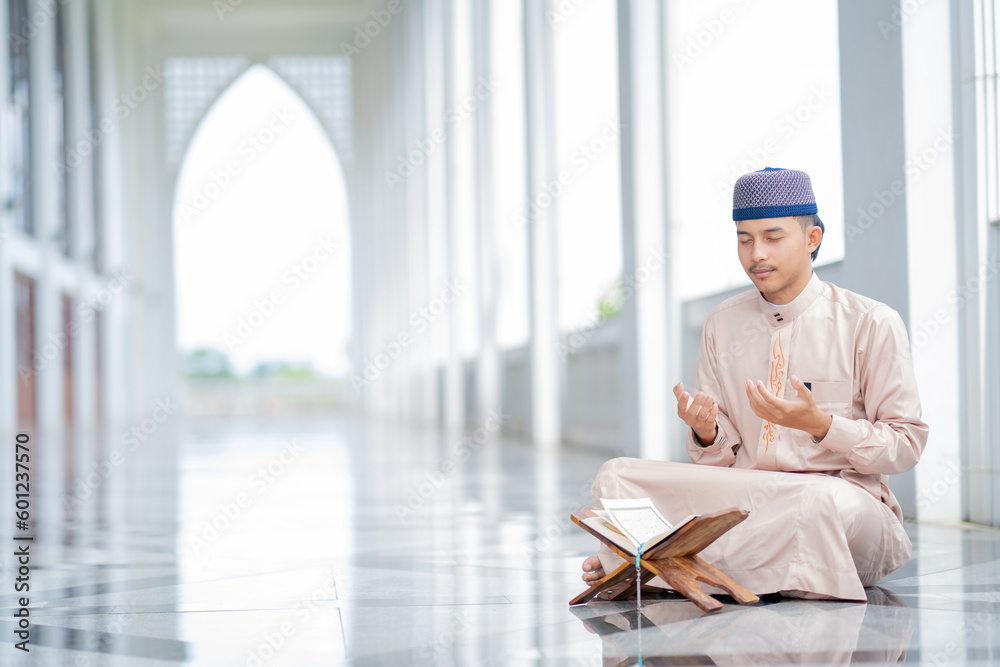 A little Asian Muslim man is sitting and reading the Quran. The peace in the mosque makes it an energetic atmosphere of faith, with copy space. A little Asian Muslim man is sitting and reading the Quran. The peace in the mosque makes it an energetic atmosphere of faith, with copy space.