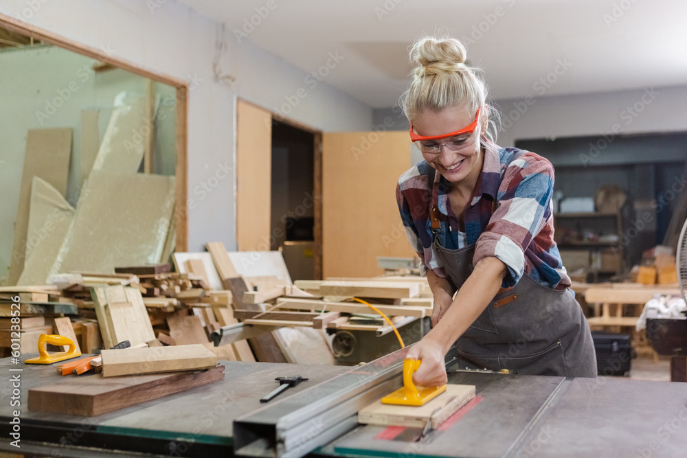 young carpenter woman wear uniform and goggles working use electronic saw cutting wood. craftsman profession in wood factory. woodworking industry. young carpenter woman wear uniform and goggles working use electronic saw cutting wood. craftsman profession in wood factory. woodworking industry.