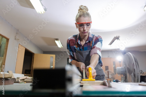carpenter woman wear uniform and goggles working use electronic saw cutting wood. craftsman profession in wood factory. woodworking industry.