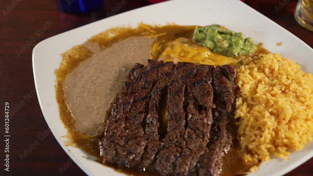 Traditional cheese enchiladas tampiquena with grilled carne asada beef on top paired with refried beans and mexican rice, slider close up 4K Traditional cheese enchiladas tampiquena with grilled carne asada beef on top paired with refried beans and mexican rice, slider close up 4K