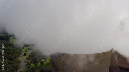 Close aerial orbit through steam cloud from coal-fired power station feat. transmission wires. Yallourn thermal power plant provides baseload electricity to Victoria, Australia by burning fossil fuels photo