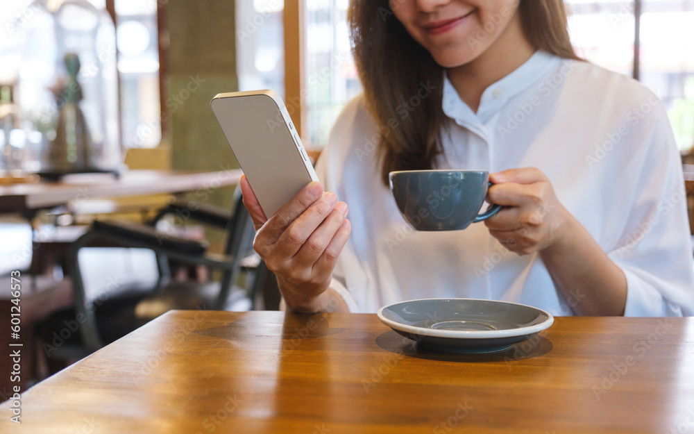 Closeup image of a young woman holding and using mobile phone while drinking coffee in cafe Closeup image of a young woman holding and using mobile phone while drinking coffee in cafe