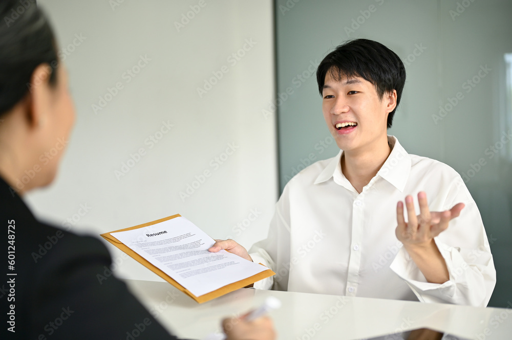 Smart young Asian male candidate telling about his career experiences to a recruiter Smart young Asian male candidate telling about his career experiences to a recruiter