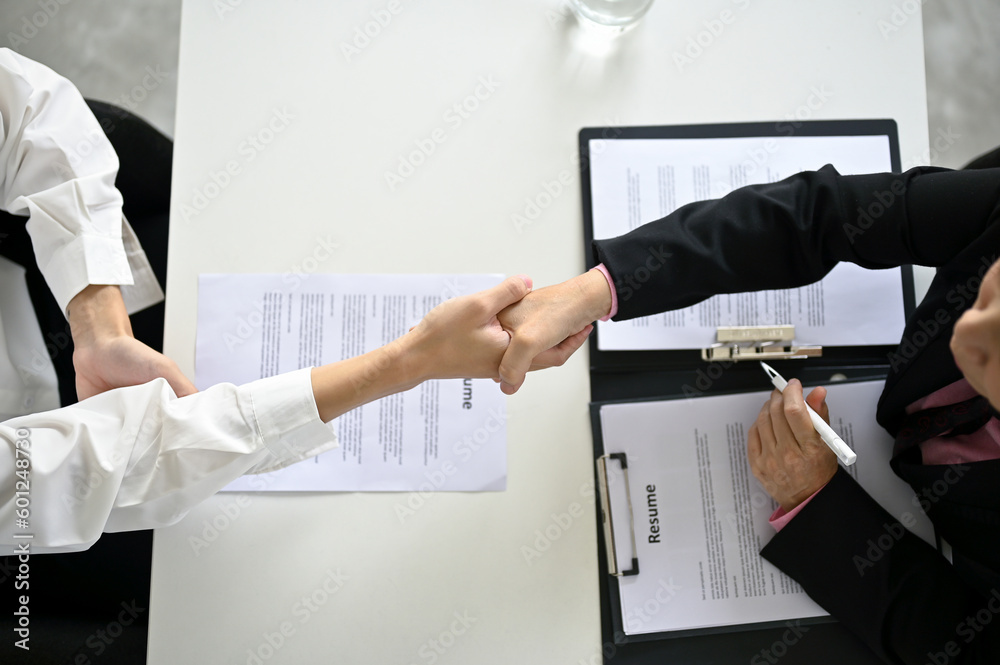 Top view of a recruiter shaking hands with a young male candidate after a job interview. - obrazy, fototapety, plakaty 