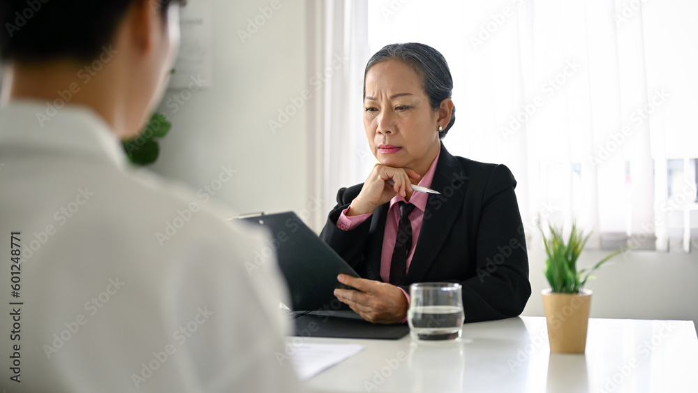 Focused senior Asian female HR manager interviewing a job candidate in the office. Focused senior Asian female HR manager interviewing a job candidate in the office.