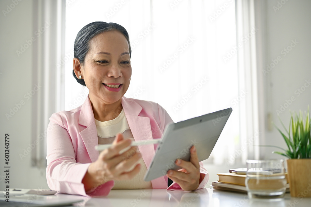Attractive senior Asian businesswoman using her tablet to manage her tasks in the office. Attractive senior Asian businesswoman using her tablet to manage her tasks in the office.