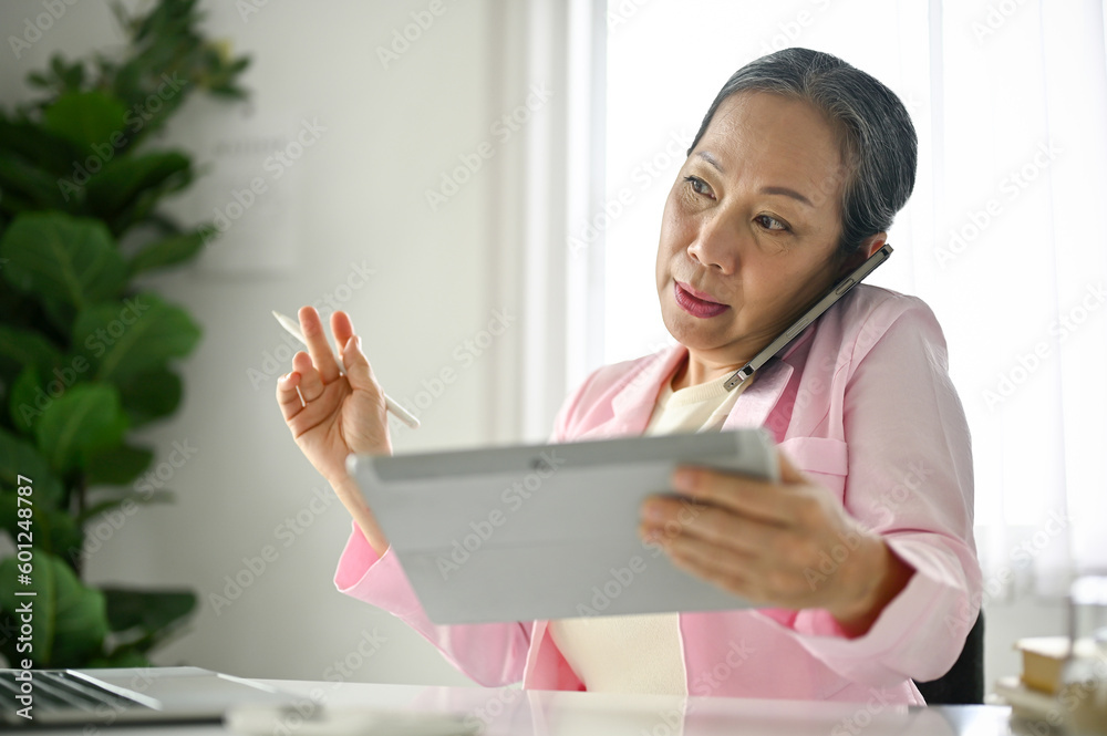 Busy senior Asian businesswoman is talking on the phone with her client Busy senior Asian businesswoman is talking on the phone with her client
