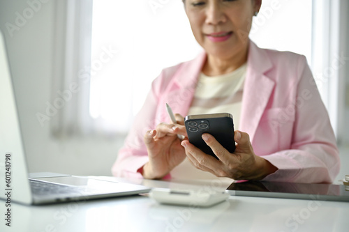 Close-up image of a senior Asian businesswoman using her smartphone at her desk.