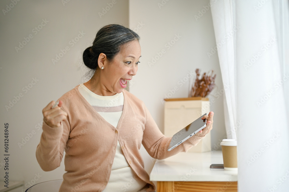Excited and surprised senior Asian woman looking at her tablet screen, screaming with joy Excited and surprised senior Asian woman looking at her tablet screen, screaming with joy