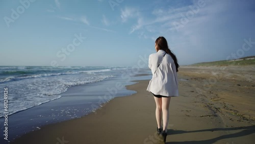 A young woman in a white jacket and black shorts, walking along the windy shoreline at sunset on a beach in Uchinada Town, Ishikawa Prefecture. photo