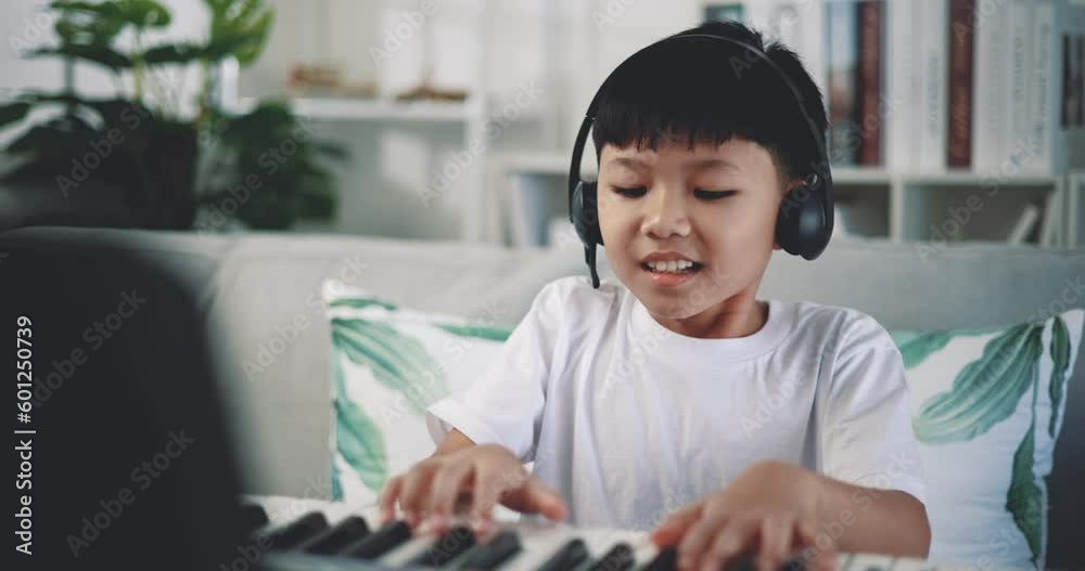 Handheld shot, Creative asian boy wearing headphone with artistic skills taking music lessons online during a video call and playing the piano at home. Music, hobby and lifestyle concepts. Handheld shot, Creative asian boy wearing headphone with artistic skills taking music lessons online during a video call and playing the piano at home. Music, hobby and lifestyle concepts.