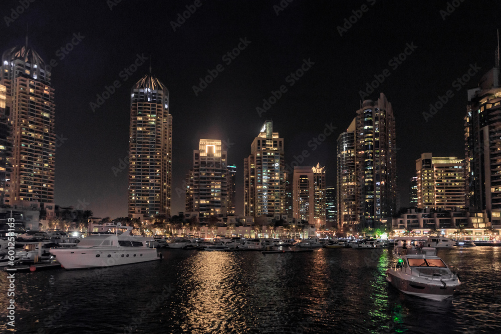 Night view from the promenade of Dubai Marina with illuminated skyscrapers, a water channel, yachts and ships in Dubai city, United Arab Emirates
