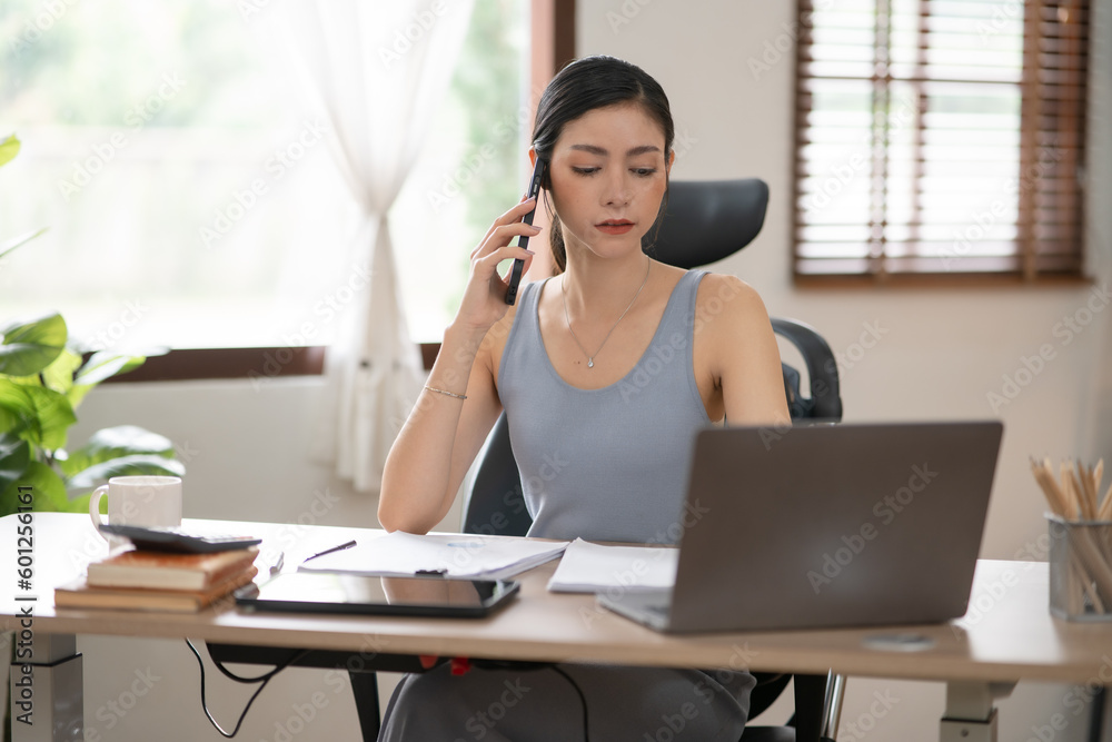 Young Asian businesswoman reading graphs and talking on phone with customers in office Young Asian businesswoman reading graphs and talking on phone with customers in office