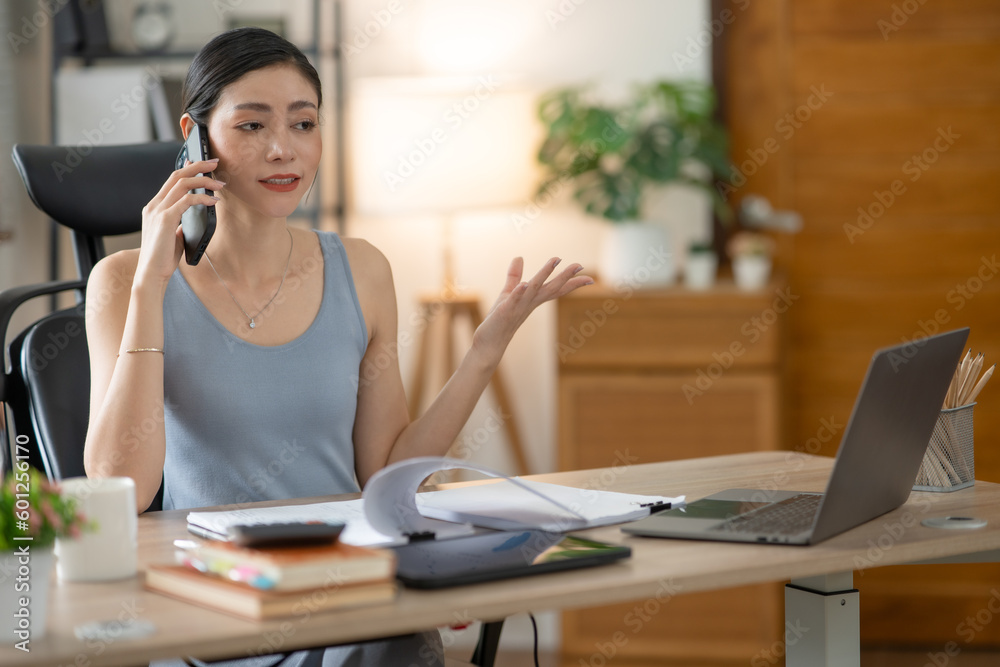 Young Asian businesswoman reading graphs and talking on phone with customers in office