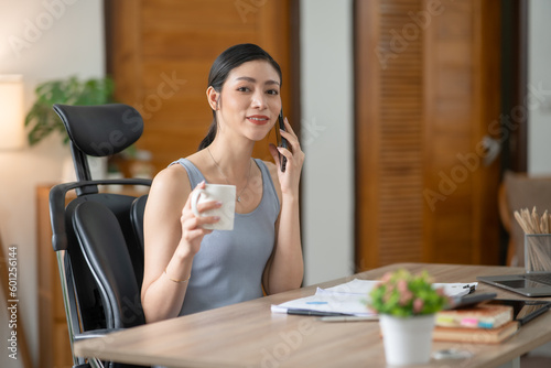Young Asian businesswoman reading graphs and talking on phone with customers in office