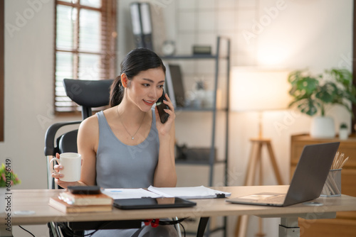 Young Asian businesswoman reading graphs and talking on phone with customers in office