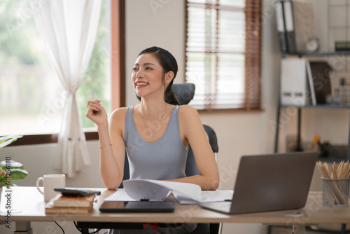 Young Asian businesswoman reading graphs and talking on phone with customers in office