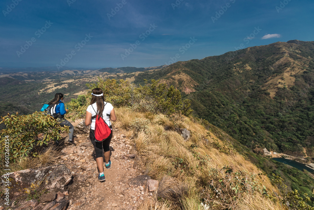 female hiker with red backpack walking along the edge of a hill on a hot sunny day in the province of Puntarenas in Costa Rica
