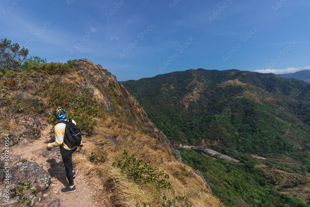 young hiker man with red backpack walking through a landscape of green mountains full of nature and countryside on a hot sunny day in the province of Puntarenas in Costa Rica