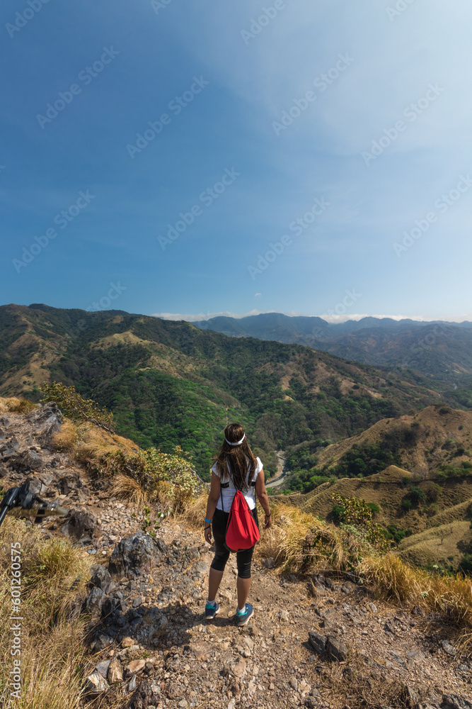 young hiker woman with red backpack contemplating the landscape of green mountains full of nature and countryside on a hot sunny day in the province of Puntarenas in Costa Rica